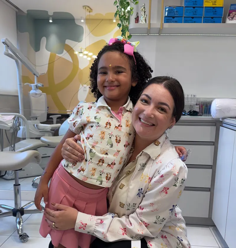Dra. Eduarda Dagostin abraçada a uma pequena paciente no consultório